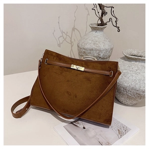Detailed close-up of brown suede shoulder bag with gold metal rotating lock and leather trim