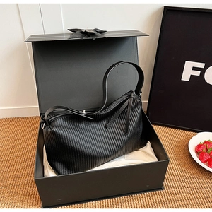 Detail of black pleated faux leather shoulder bag presented in an elegant gift box