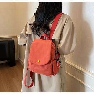 Rear view of a model wearing the orange canvas mini backpack with a yellow button detail