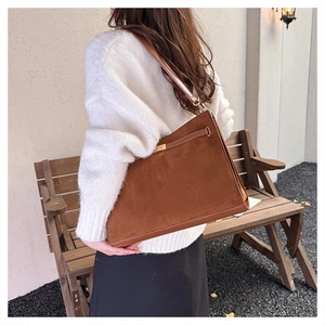 Detail view of a brown suede trapezoid shoulder bag featuring a gold metal lock closure