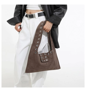 Détail du sac hobo en daim marron avec œillets métalliques porté sur un blouson en cuir