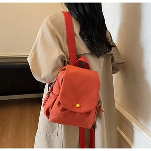 Detail view of small orange-red canvas backpack featuring round yellow buckle and wide straps
