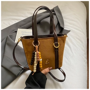 Dettaglio della borsa a secchiello in pelle scamosciata con logo dorato e nappa