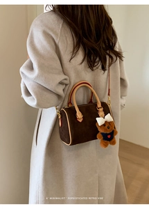 Detail of dark brown suede boston bag with bear charm worn by woman in beige coat