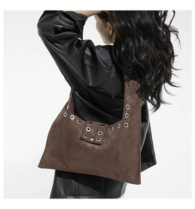 Détail du sac bandoulière en daim marron foncé avec œillets métalliques et style punk