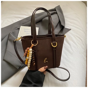 Dettaglio della borsa a secchiello in pelle scamosciata marrone con logo dorato e perline