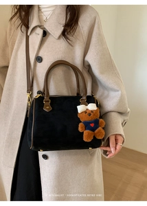 Detail view of a black suede Boston bag with a teddy bear charm and brown leather straps