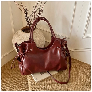 Detail of burgundy waxed leather tote bag with drawstring sides on a woven rug