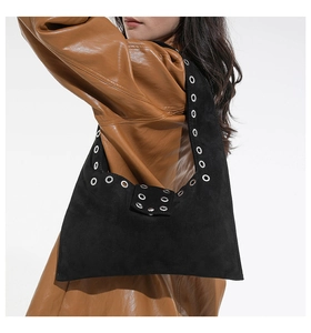 Détail du sac hobo en daim noir avec rivets argentés porté avec un manteau en cuir