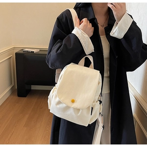 Detail of a cream canvas backpack with yellow buckle and side drawstring pocket worn by model