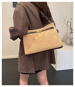 Detail view of brown suede tote bag with golden lock and leather trim on female shoulder