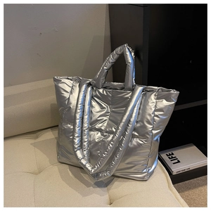 Detailed view of silver quilted down tote bag with dual handles on a stylish sofa