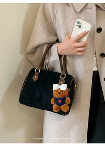 Detail of retro black suede Boston bag with brown handles and cute plush bear charm