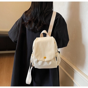 Detailed back view of a minimalist cream canvas backpack on a model wearing black