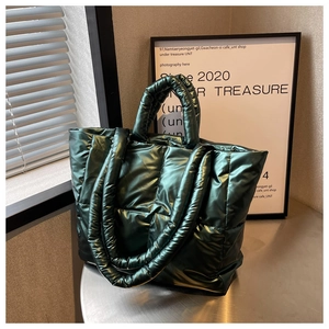 Detail of dark green quilted puffer tote bag with metallic texture on a round table