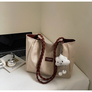 Beige suede tote bag with woven straps and a plush cloud charm on a desk