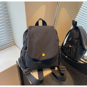 Detail view of black canvas mini backpack with yellow snap button and mirror reflection