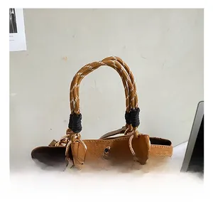 Detail van bruine suède handtas met gevlochten touwhandvat en een glinsterend strikmotief