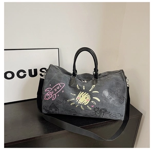 Detail of dark grey canvas duffel bag featuring colorful graffiti prints and leather handles