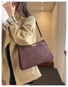Detail of dark brown matte suede shoulder bag with gold twist lock on a beige trench coat