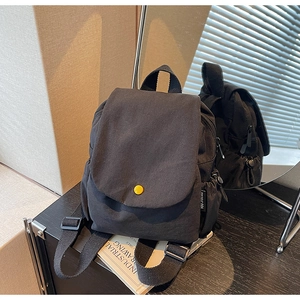 Detail of black canvas mini backpack featuring a yellow button and side drawstring pocket