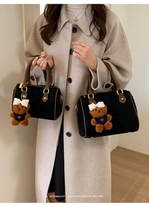 Close-up of retro black suede pillow bags in two sizes held by a model wearing a coat