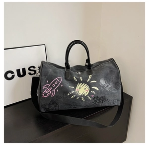 Detail of black canvas duffel bag featuring colorful graffiti prints and leather handles