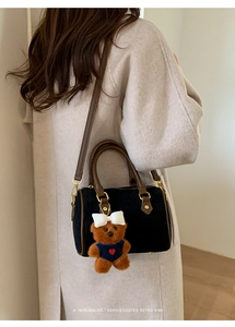 Detail of a vintage black suede Boston bag with brown leather handles and bear charm