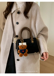 Close-up of black suede Boston bag featuring brown handles and a cute bear charm