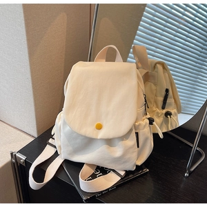 Detail of minimalist canvas mini backpack showing yellow button and side pocket features