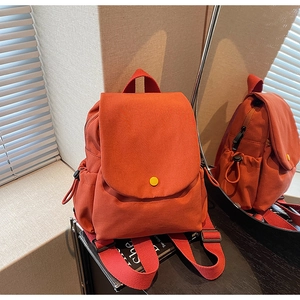Detail view of the vibrant orange canvas backpack featuring a flap cover and side pockets