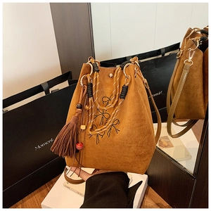 Détail du sac seau en daim marron avec nœud brodé et pompon à franges vintage