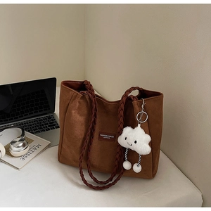 Detail of a brown suede tote bag with woven handles and a soft cloud-shaped plush charm