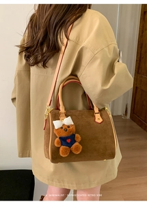 Macro shot of brown suede boston bag featuring cream leather handles and a plush bear charm