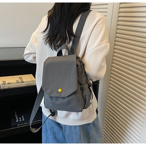 Detail view of a dark grey canvas backpack with a yellow button and drawstring pockets