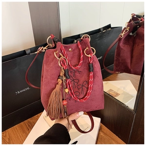 Détail du sac seau bordeaux en daim avec poignée tissée, gland et nœuds en strass