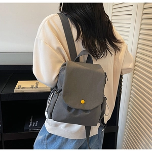 Close-up of grey canvas backpack featuring a distinctive yellow button and drawstring side pockets
