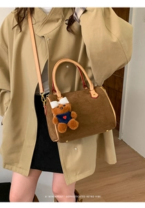 Close-up of brown suede boston bag with leather straps and a cute teddy bear charm