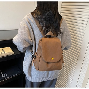 Detail of brown canvas backpack featuring drawstring side pockets and contrast yellow button