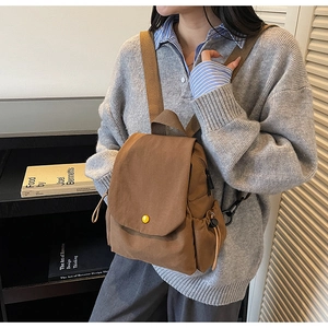 Detail view of brown canvas backpack with flap closure and a yellow button accent