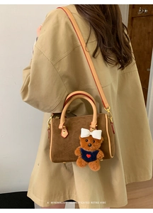 Close-up of brown suede pillow bag with a cute bear charm and red edge detailing