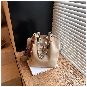 Détail du sac seau en daim beige avec motif de nœud et pompon à franges décoratif
