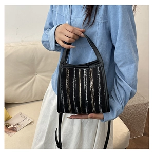 Detalle de bolso tejido de rayas verticales con ribetes de cuero negro y correa ajustable