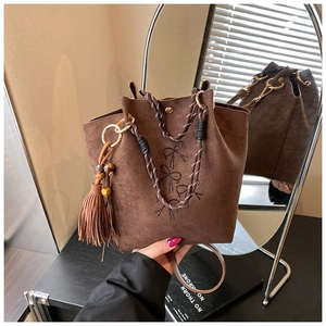 Détail du sac seau en daim marron café avec nœuds en strass et poignée tressée