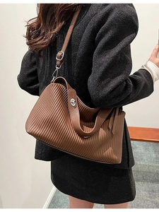 Brown pleated tote bag with silver twist lock shown on model in grey suit attire