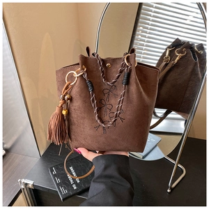 Détail du sac seau marron en suédine avec poignée tissée et grand pompon décoratif