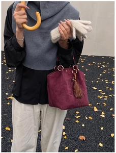 Détail d'un sac seau en daim bordeaux avec de longues franges et des perles en bois