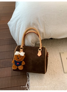 Brown frosted Boston bag featuring a plush teddy bear charm on a cozy rug setting