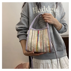 Detalle de bolso tipo cubo tejido a rayas con correa de cuero lila llevado por una modelo