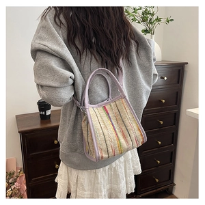 Detalle de rayas tejidas de colores en un bolso cubo con asa y correa de cuero púrpura